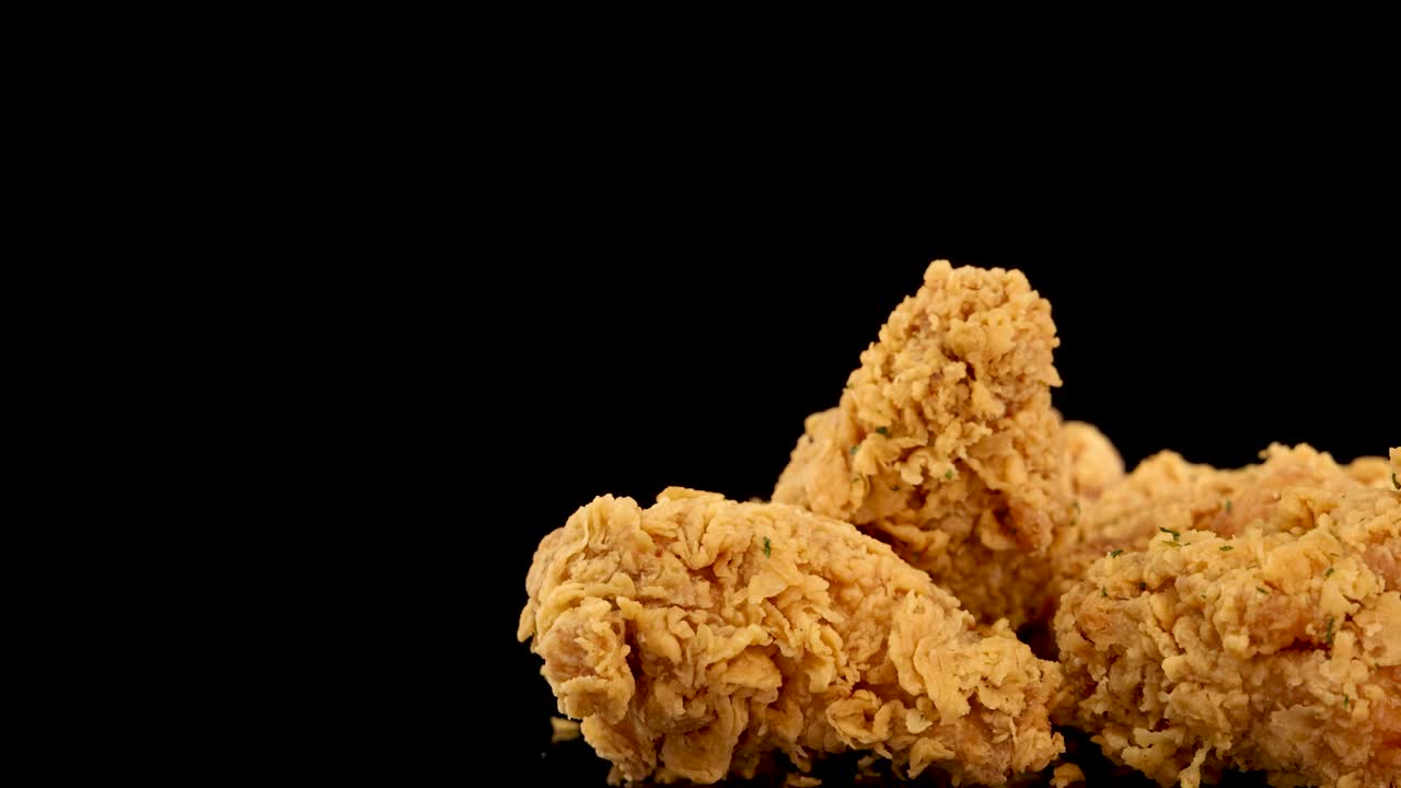 Golden, crumbed fried chicken breasts and thighs rotate in slow motion against a black background, with dramatic lighting and a gradual zoom-in effect