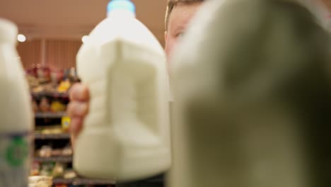 Un-Serio-Trabajador-De-Supermercado-Con-Sobrepeso,-Con-Una-Camiseta-Blanca-Y-Un-Delantal-Negro,-Coloca-Grandes-Botellas-De-Plástico-De-Leche-En-Un-Estante-Del-Supermercado