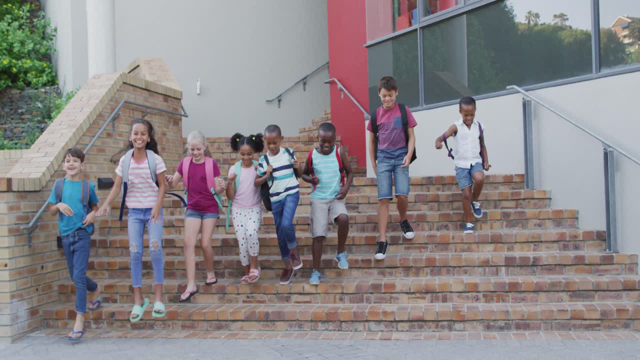 Diverse group of schoolchildren wearing backpacks smiling and running downstairs after school