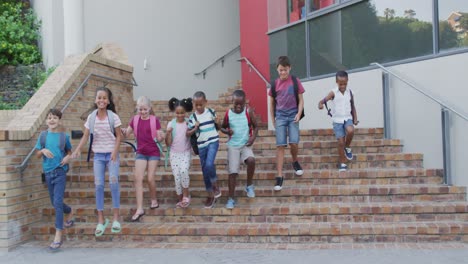 diverse group of schoolchildren wearing backpacks smiling and running downstairs after school