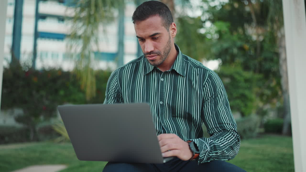 Young man using laptop sitting in bench outdoors.