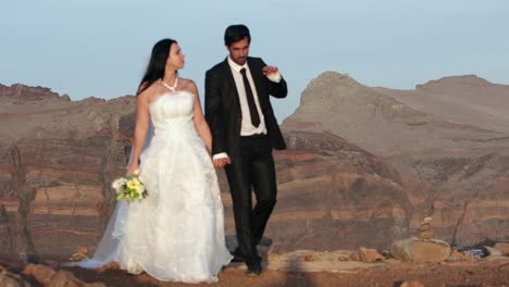 newly married couple holding hands walking on volcanic rocks talking at sunset on wedding day at remote seaside coastal location celebrating love bridal photoshoot panaromic natural color grade slowmo