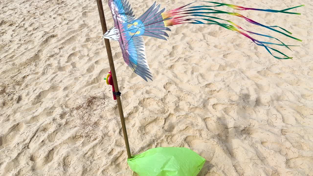 Vista en picado de una cometa de pájaro vibrante revoloteando sobre la arena en una playa soleada