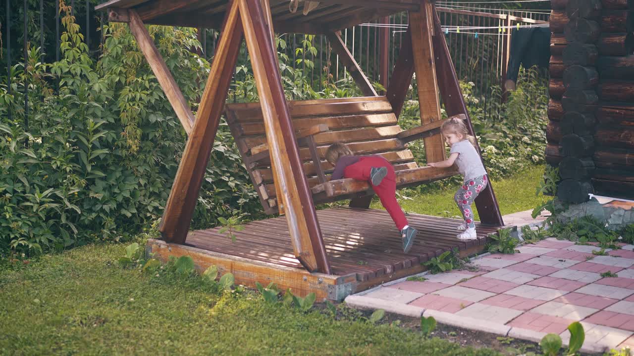 Bambini che si dondolano su una grande altalena di legno vicino alla casa estiva dove giocano.