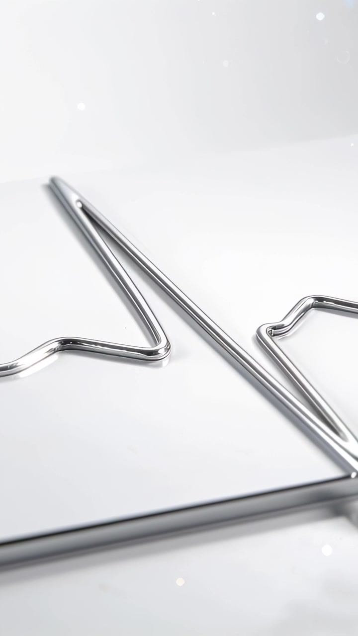 Vertical video: Tilting camera centering chrome wire on white surface, revealing bar and sparks