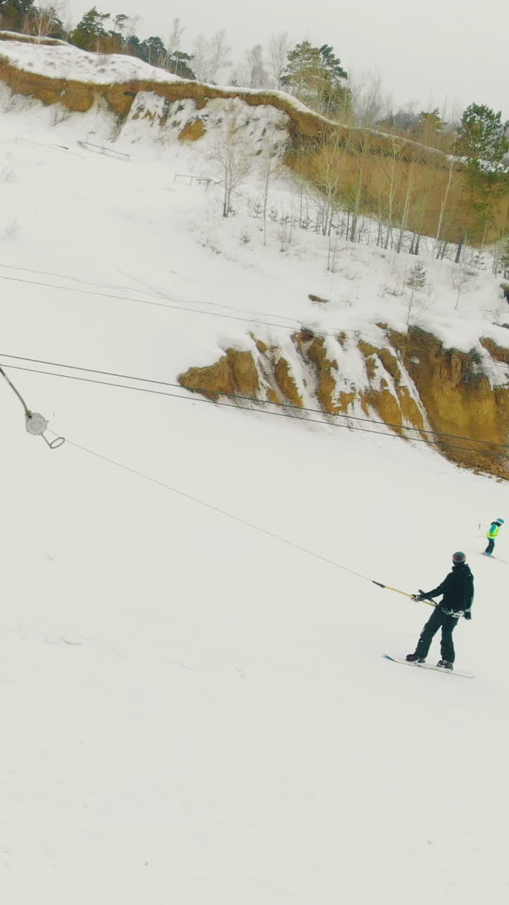 person on skies rises on snowy hill with electric surface t-bar lift at modern winter resort with wide track aerial view