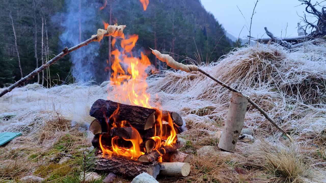Grilling bread on sticks over campfire outdoors in frozen landscape