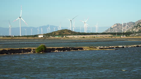 wind turbines spinning in wind farm, river lake water flowing in foreground