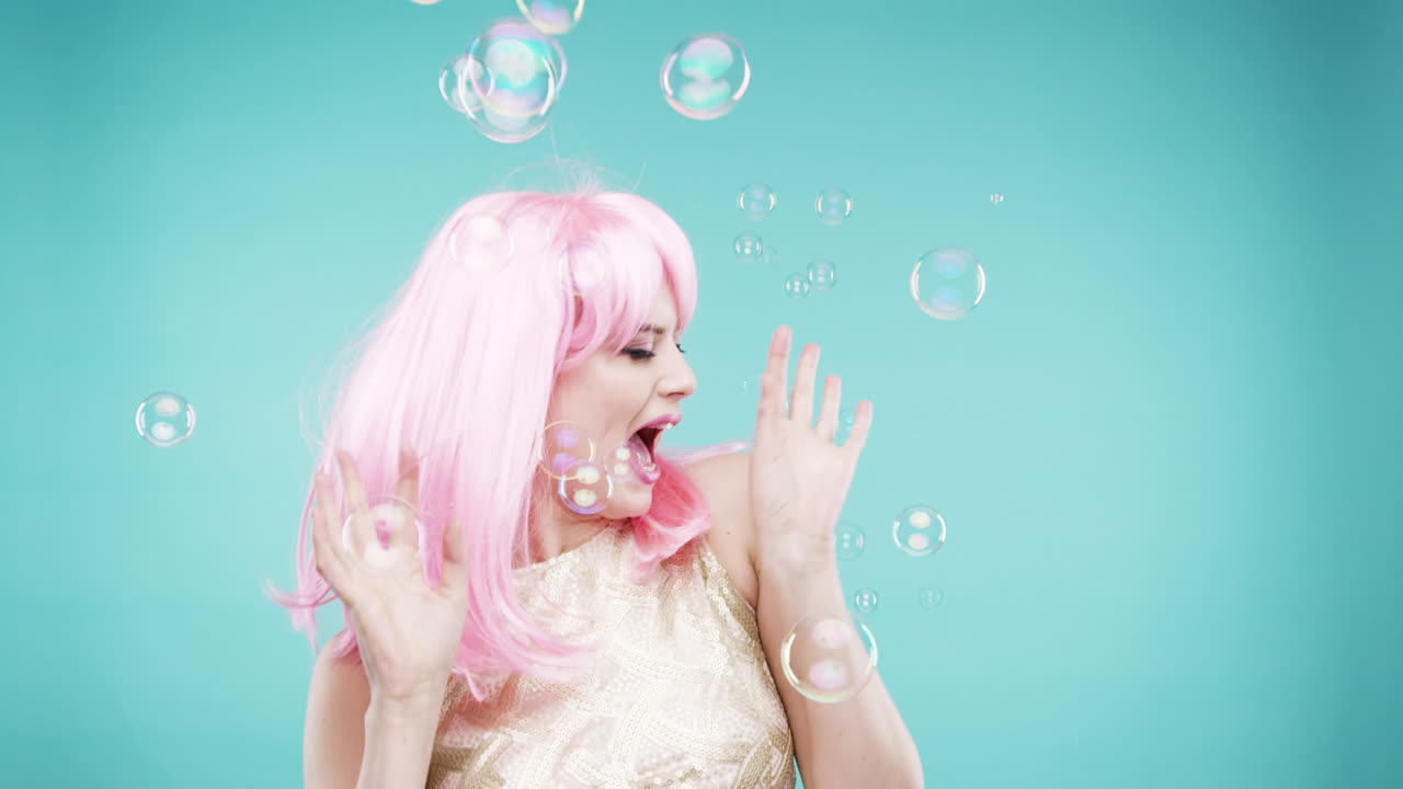 cara loca mujer de cabello rosa bailando en duchas de burbujas cabina de fotos de movimiento lento fondo azul