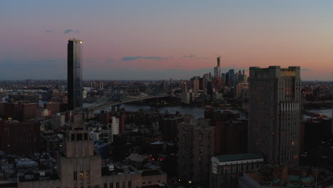 Aerial-descending-footage-of-town-development-in-Lower-Manhattan.-View-of-bridges-and-high-rise-buildings-in-Brooklyn-in-twilight-time.-Manhattan,-New-York-City,-USA