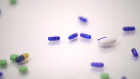 macro de cámara lenta de variedades de píldoras deslizándose sobre una píldora azul y amarilla sobre fondo blanco