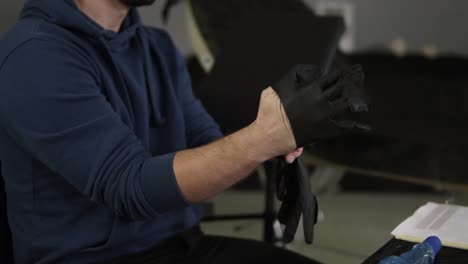 close up de manos artista del tatuaje poniendo los guantes negros de látex antes de una sesión de tatuaje en la tienda de tatuaje. tatuador sentado en una silla en el salón sala de paredes grises. fondo borroso. cámara lenta