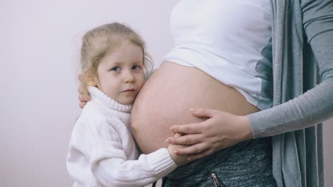 chica bonita acaricia a madre embarazada con gran vientre en la habitación