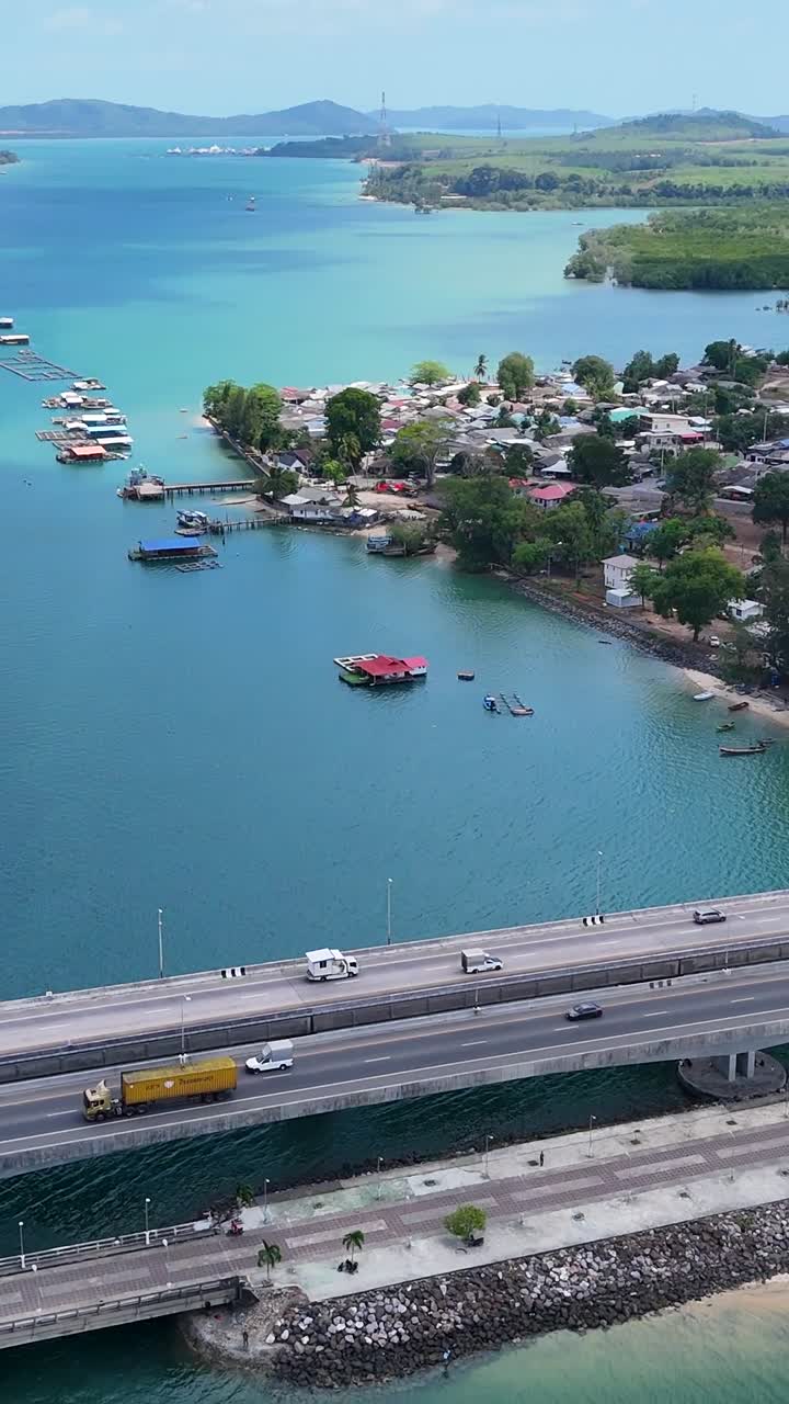 드론 영상은 태국 푸켓의 사라신 다리를 포착합니다. 푸른 하늘 아래 푸른 푸른 물과 멀리 있는 산을 가로질러 펼쳐져 있습니다.