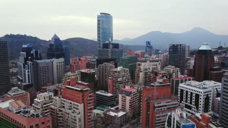 Vogelperspektive-Auf-Das-Finanz--Und-Wohnzentrum-Von-Santiago,-Chile,-Mit-Dem-Titanturm-Und-Mehreren-Backsteingebäuden,-Bergen-Im-Hintergrund-Mit-Leichtem-Dunst