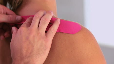 Physiotherapeut-Legt-Rosa-Kinesiotape-Auf-Den-Rücken-Des-Patienten