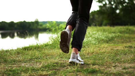 primer plano de pies corriendo en zapatillas a lo largo del río en el césped