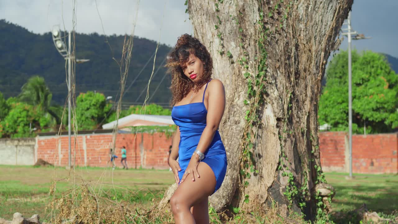 Una ragazza dai capelli ricci con un vestito blu corto si gode un parco tropicale sull'isola caraibica di Trinidad