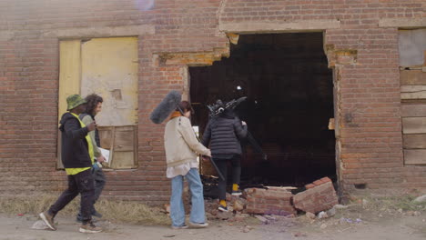 four coworkers holding material for a recording as they enter a ruined building 1