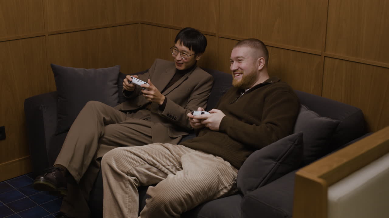 두 남자가 소파에서 비디오 게임을 하고 있다.