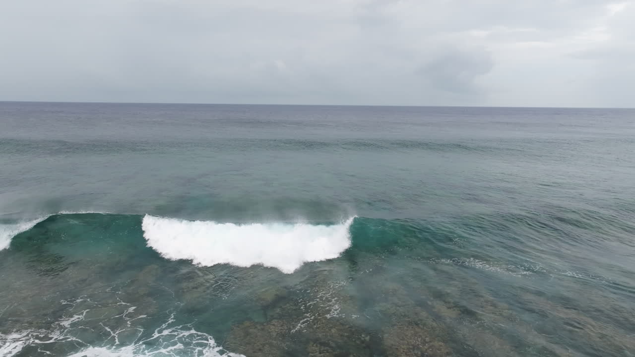 Aerial pullback frontal view of waves breaking on shallow fringing reef in ocean water