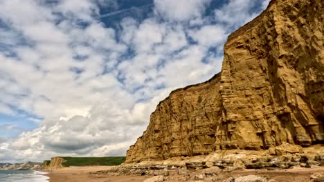 slow motion footage of a black bird flying in front of a jurassic coast cliff face in dorset. the bird flying from right to left with clouds above. impressive golden cliff face.