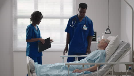 senior patient on bed talking to 2 african american doctor in hospital room health care and insurance concept. doctor comforting elderly patient in hospital bed or counsel diagnosis health.