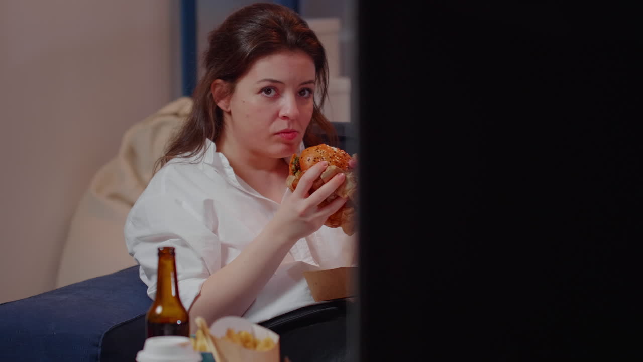 Business woman watching TV eating burger in living room