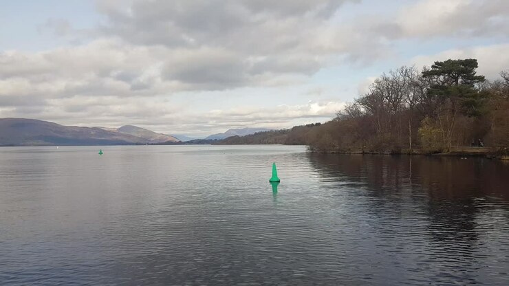 Ripresa da una barca che scivola sul Loch Lomond nel Parco Nazionale dei Trossachs in Scozia in una nuvolosa giornata invernale, catturando la bellezza malinconica delle Highlands