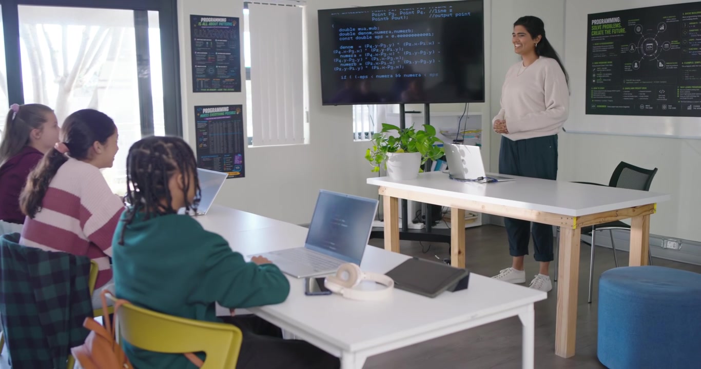 Indian teacher leading 3 female teens teaching using laptop in workshop nodding to raised hand