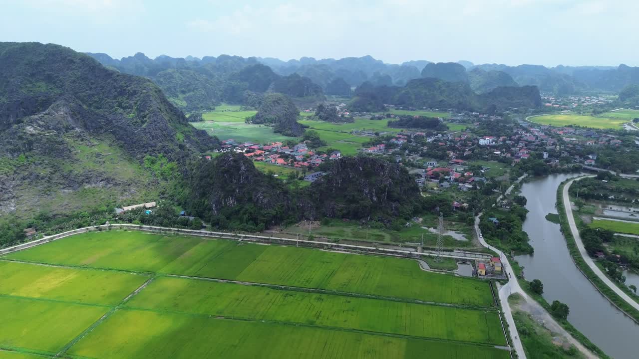 Aerial zoom in over patchwork rice fields and a village nestled among karst hills in northern Vietnam