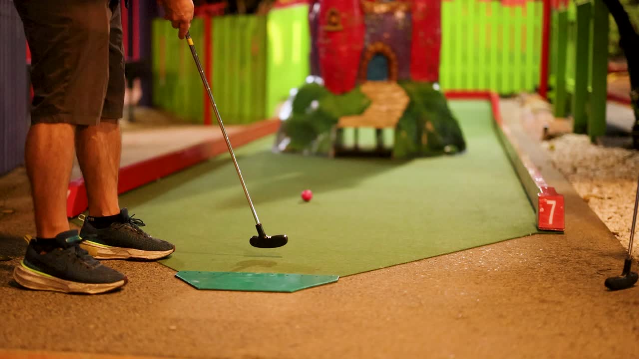 A person attempts a putt on a mini-golf course, humorously missing the hole. Bright, colorful environment with playful atmosphere