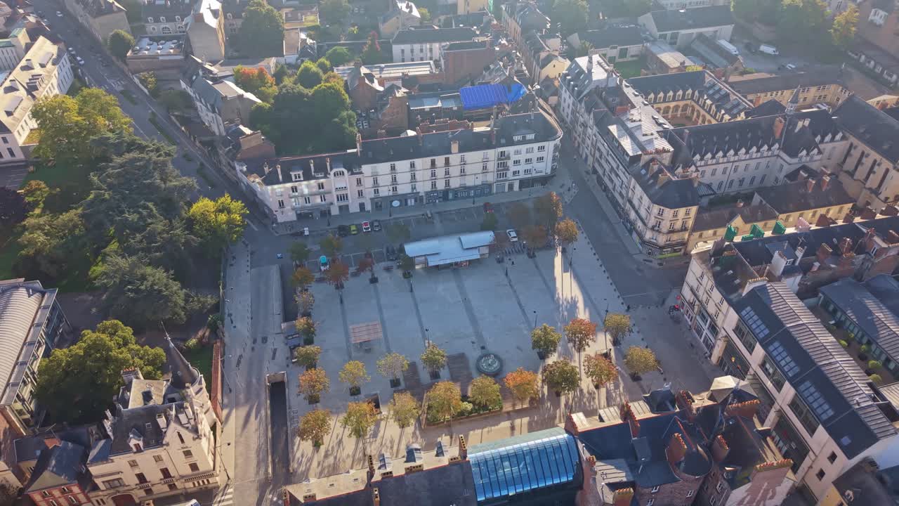 Drone shot in near top-down view over Place Hoche in Rennes, showing sunlit buildings, trees and the surrounding cityscape