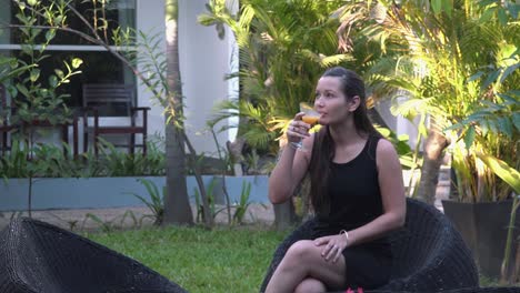 Plano-Medio-De-Una-Hermosa-Joven-Jugando-Con-Una-Flor-Mientras-Disfruta-De-Un-Cóctel-En-Los-Terrenos-Del-Hotel-Tropical