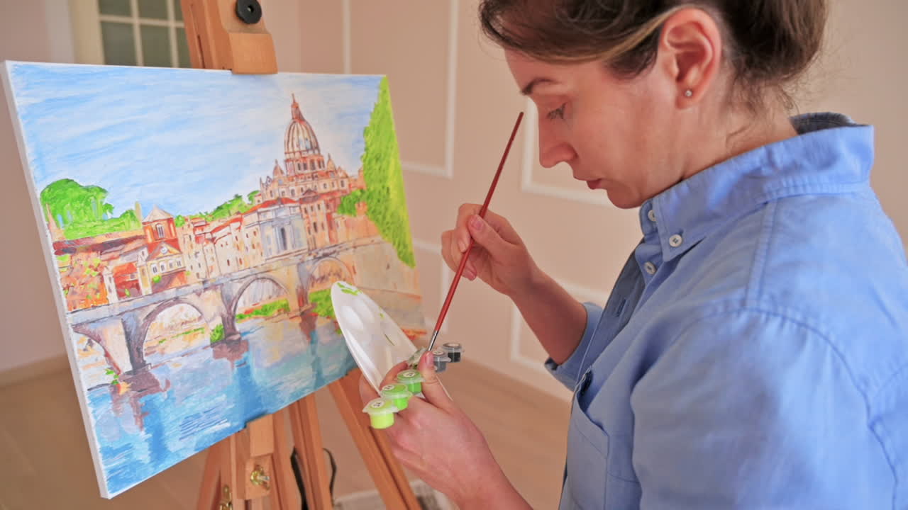 Woman mixing paints on a palette and painting picture on the easel at home. Slow motion