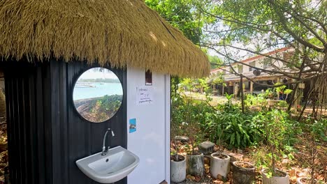 a rustic outdoor toilet with a thatched roof amidst lush greenery in phuket, thailand, captured in bright daylight