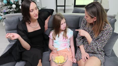 women and a girl relaxing on a sofa, enjoying chips and conversation