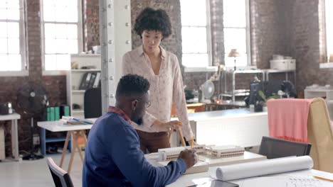 Focused-diverse-architect-colleagues-discussing-work-with-building-model-in-office-in-slow-motion