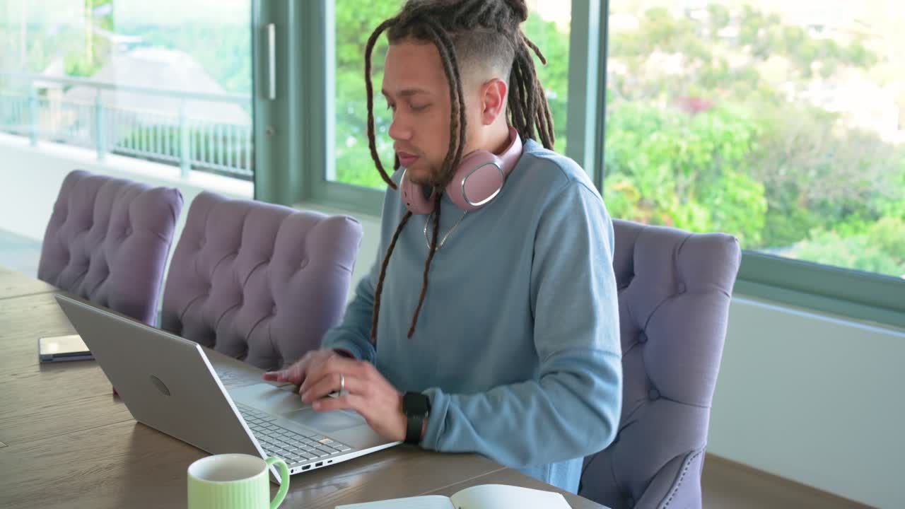 Mid-adult African American man typing on silver laptop at table then stretching for tension relief