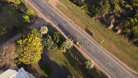 Aerial-birds-eye-shot-of-Tractor-crane-Vehicle-driving-on-road-in-Punta-del-Este-Beach,Uruguay---Car-overtaking-on-road-at-sunset---orbit-shot