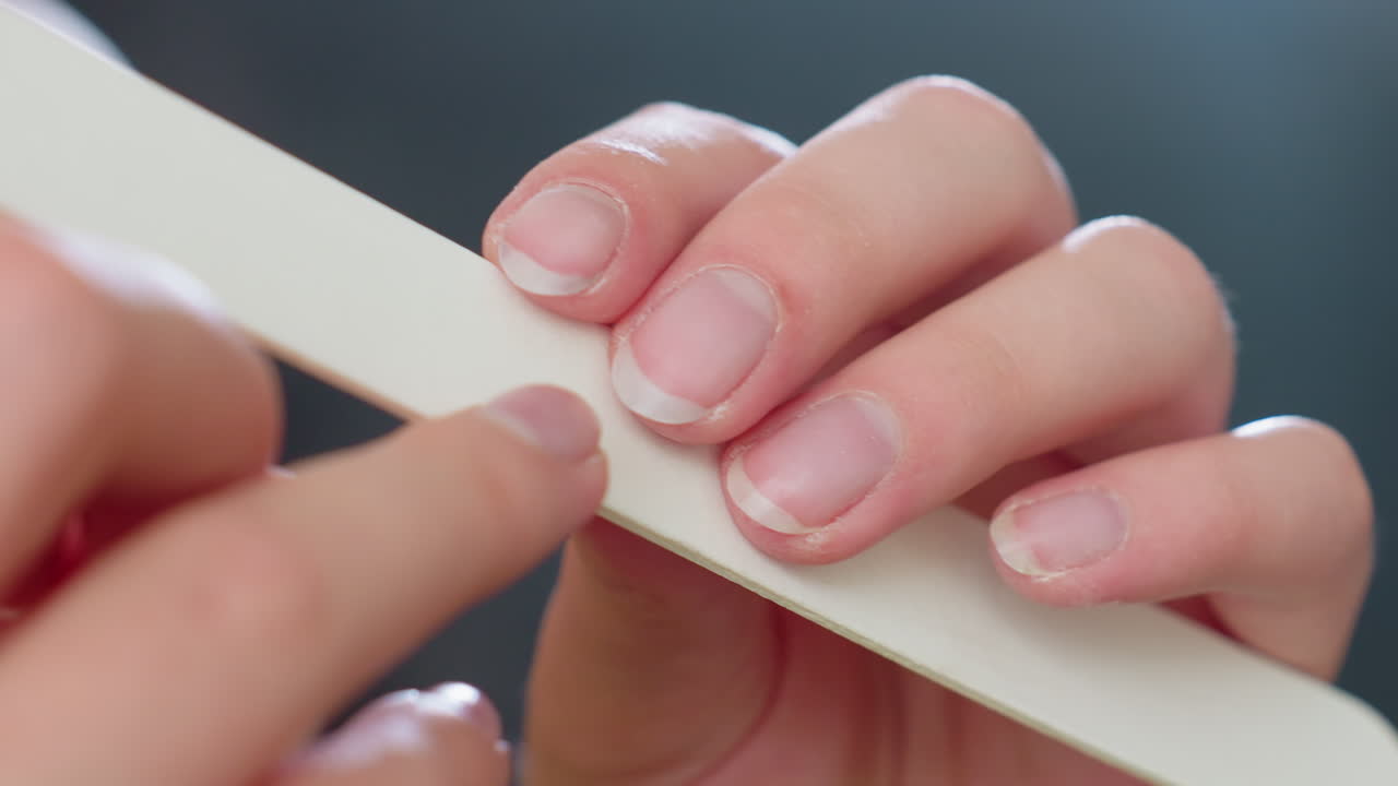 Extreme close up view of woman filing fingernails with white nail filer, focusing on natural nail edges and grooming process, capturing detail of personal hygiene and home manicure care routine