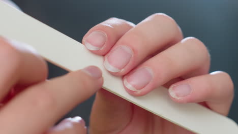 extreme close up view of woman filing fingernails with white nail filer, focusing on natural nail edges and grooming process, capturing detail of personal hygiene and home manicure care routine