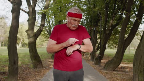 Senior-old-man-running-in-park-and-using-smart-watch,-tracking-result-after-fitness-workout