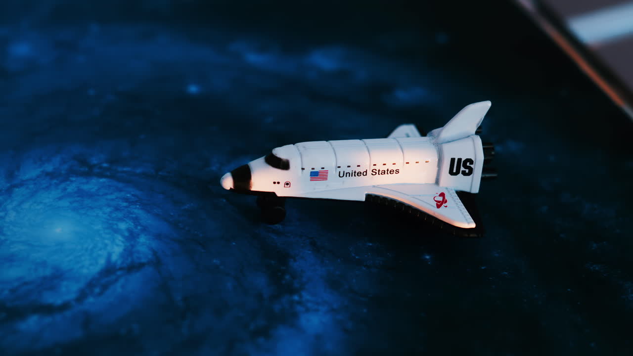 Close up of a miniature toy space shuttle placed on a blue cosmic galaxy backdrop