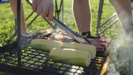 turning over lamb chops on a smokey backyard campfire bbq in the late afternoon