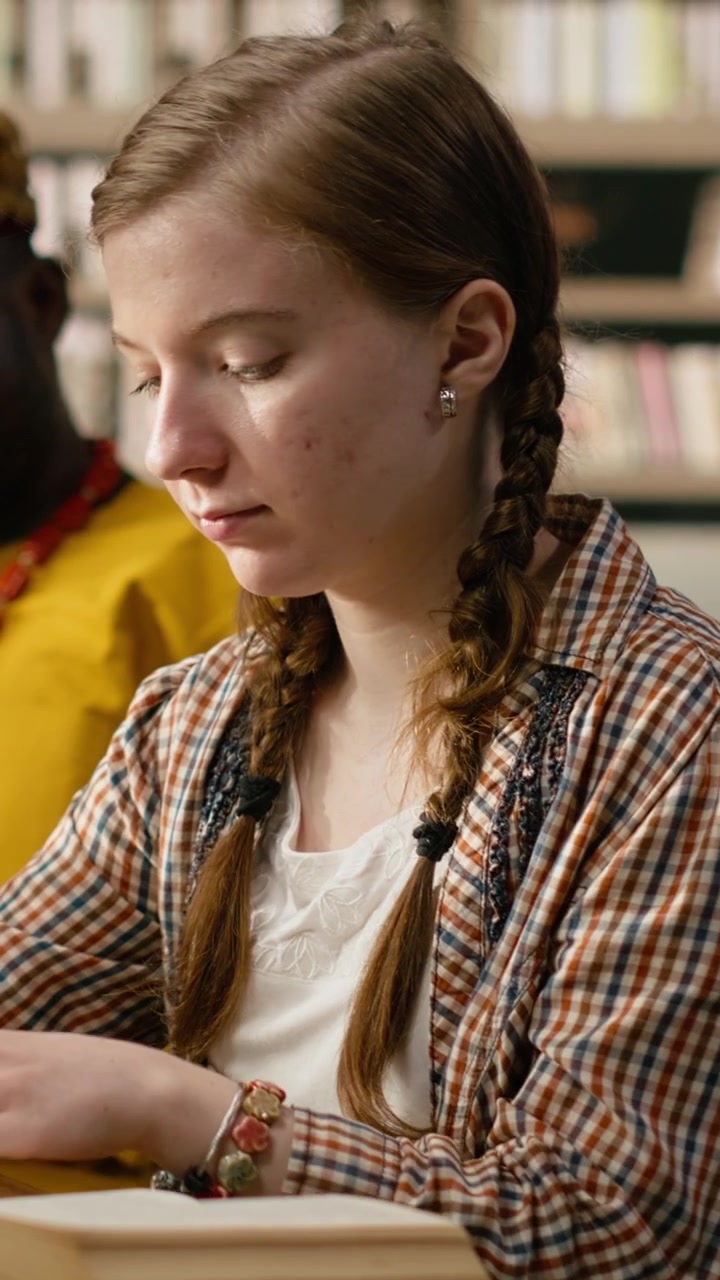 Vertikal video: Ung kvinnelig student jobber ved bibliotekpult med bærbar PC og stabel med bøker