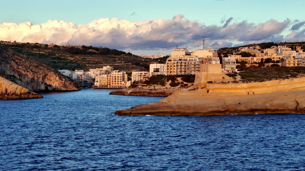 Tramonto dorato sull'incantevole villaggio costiero e sulle scogliere calcaree di Xlendi Bay, Gozo, Malta. Xlendi Bay a Gozo al tramonto, che mette in risalto la calda luce dorata che colpisce