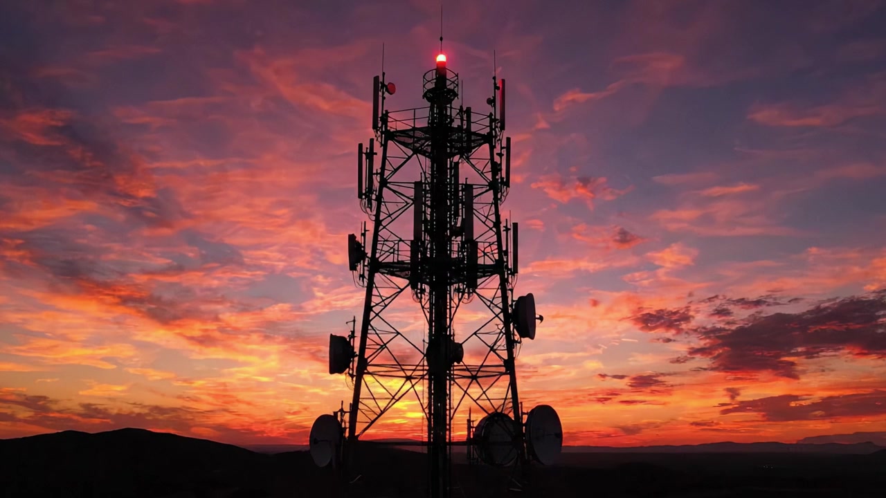 Betagende solnedgang over en tårnhøj kommunikationsstruktur: En smuk silhuet mod en levende himmel med nuancer af orange, pink og lilla