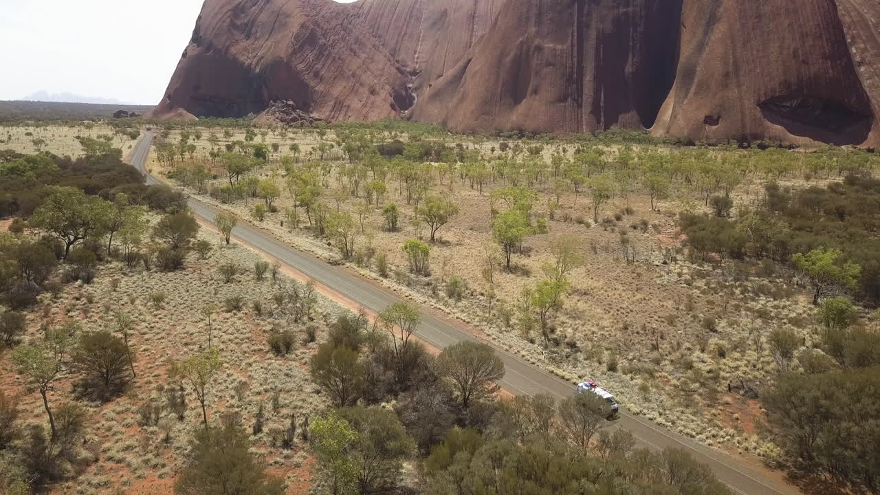 Drone flying over a white campervan driving alongside Uluru-Ayers Rock