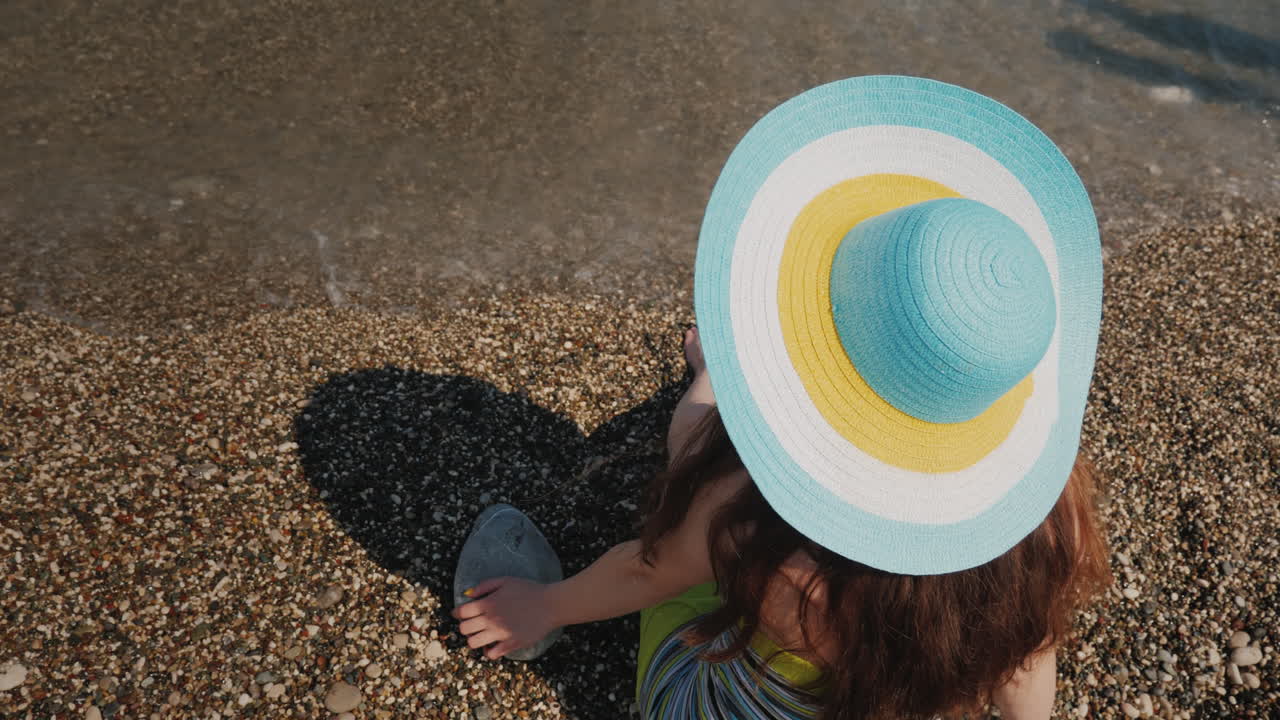 una joven con el pelo largo y oscuro con un sombrero textil de colores brillantes se sienta en la vista de la costa desde el